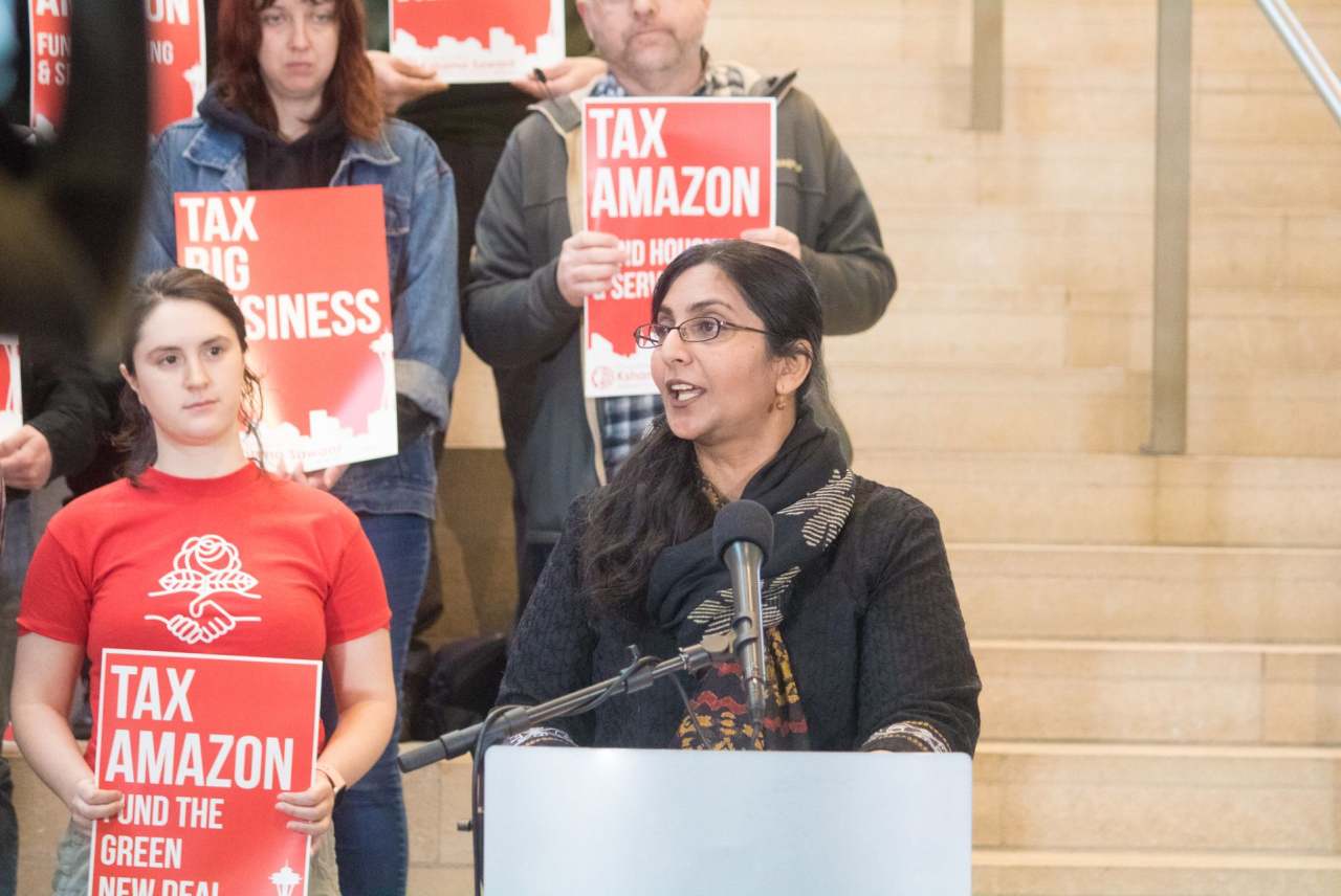 Speaker and protestors holding placards with 'Tax Amazon' wording