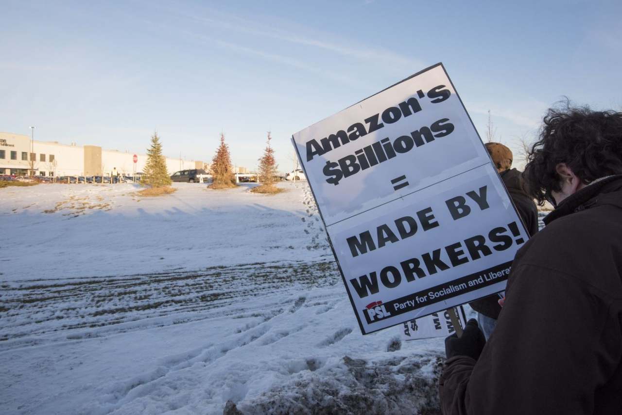 Person protesting about AMazon. Placard reads 'Amazon's billions are made by workers'