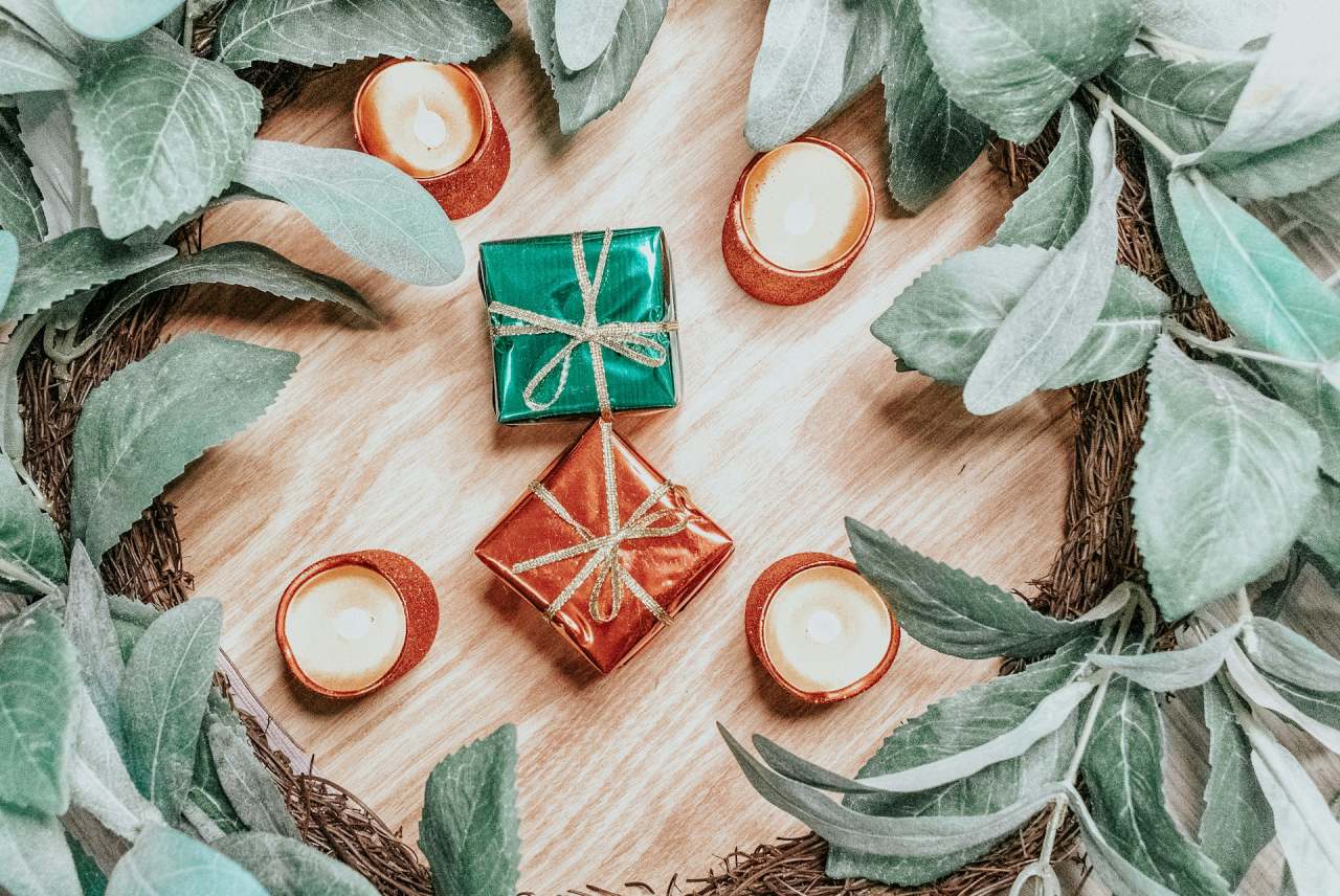 Wreath with greenery on table, small gifts and candles in the middle