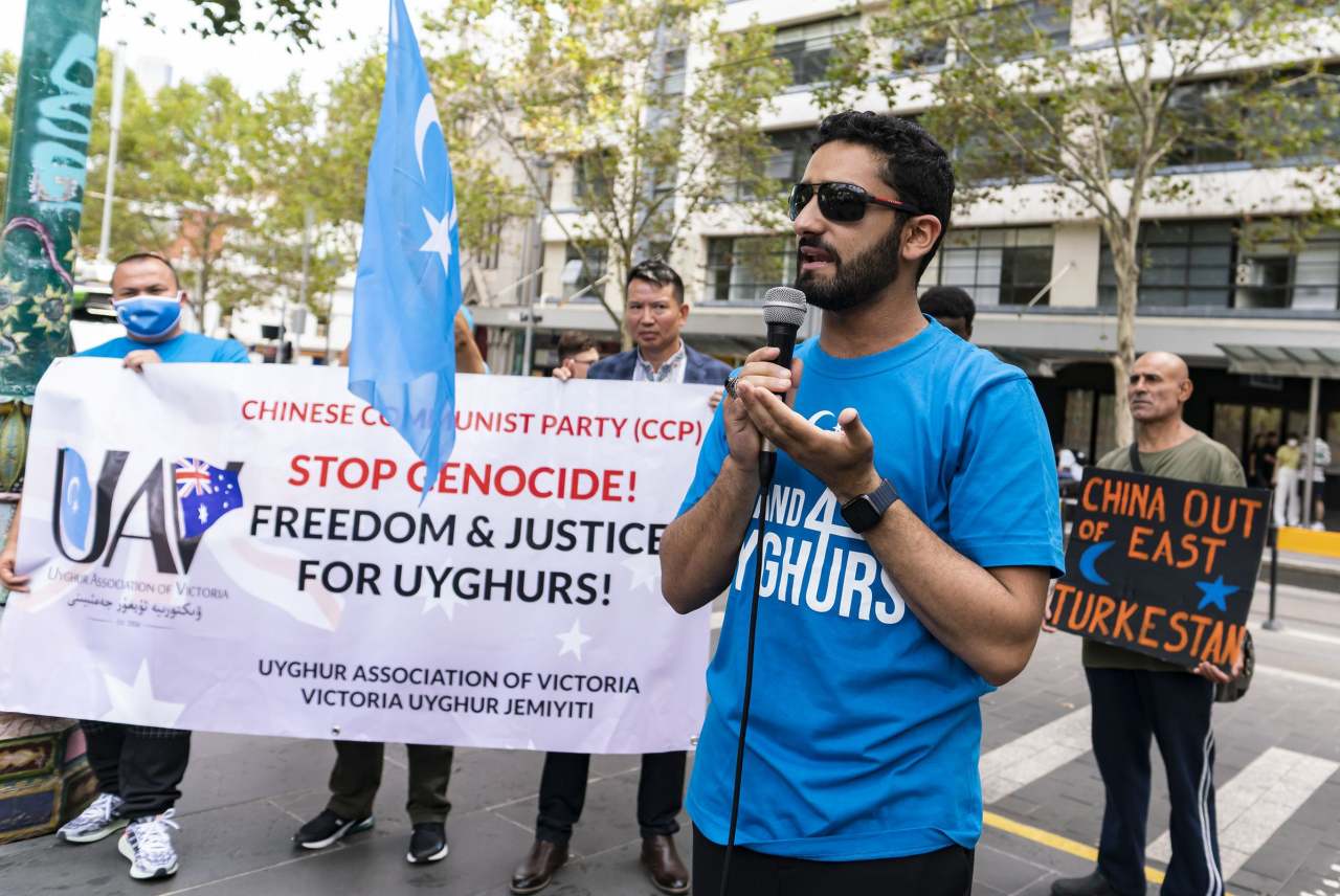 People speaking at rally, with freedom for Uyghurs banner