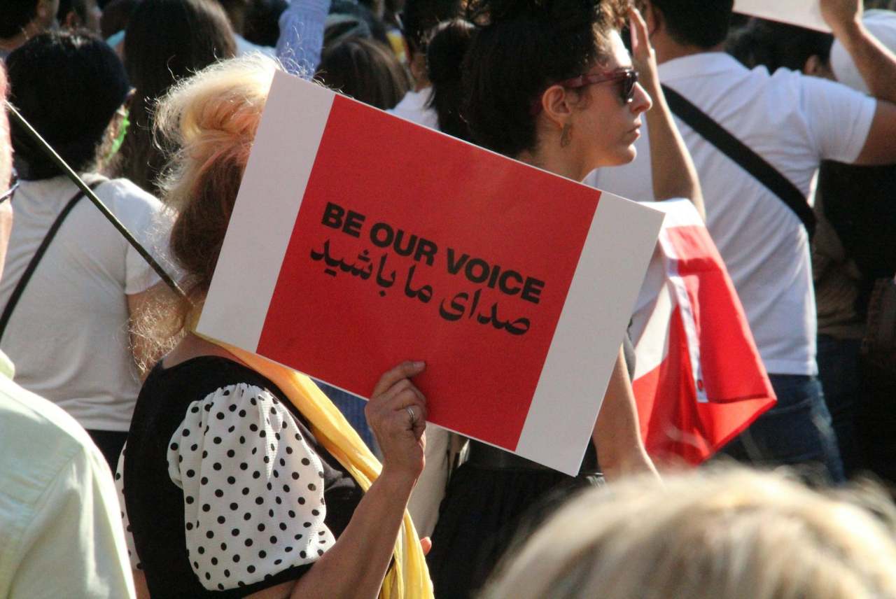 Crowd of people, one placcard reads 'Be our voice' with this also in Arabic
