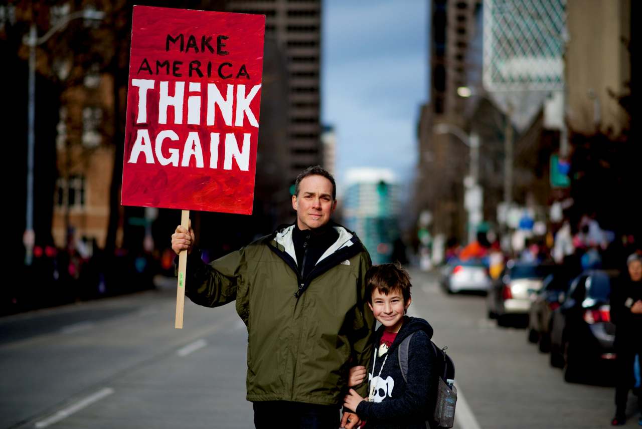 Man and boy on street holding sign which reads 'Make America Think Again'