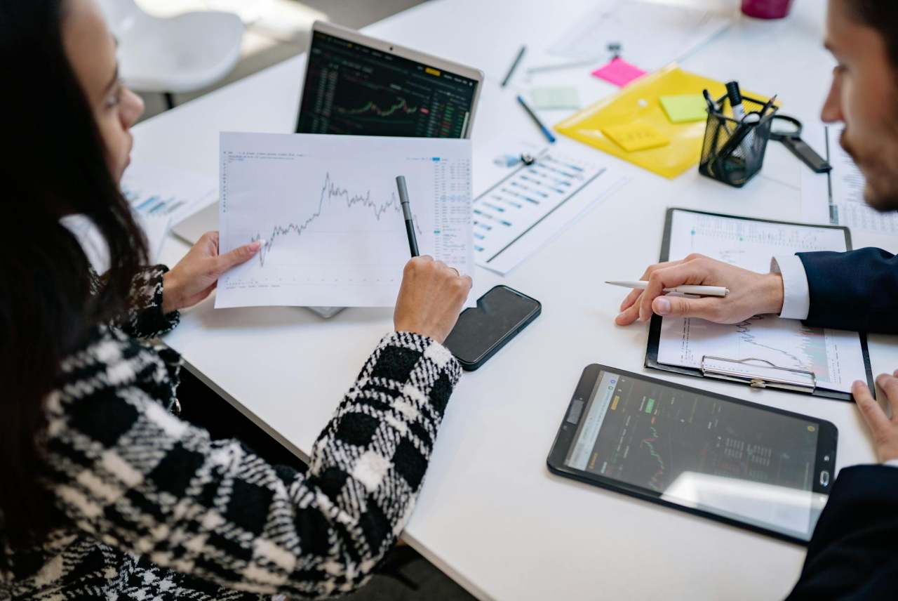 Women pointing at line graph on paper sat at desk with man