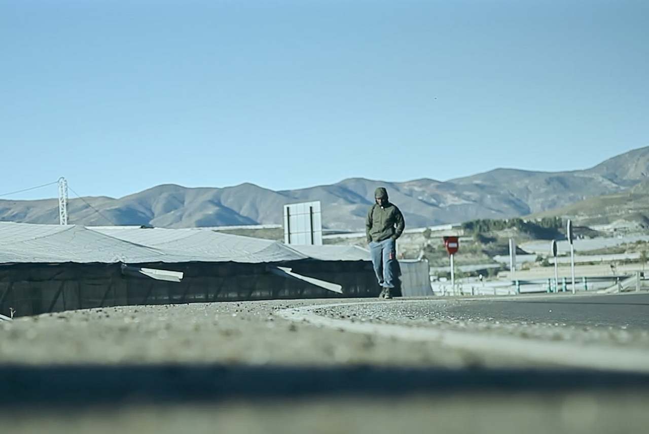 A worker walks next to low-rise building, with mountains in background