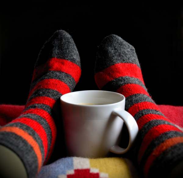 Feet in warm socks around a hot cup